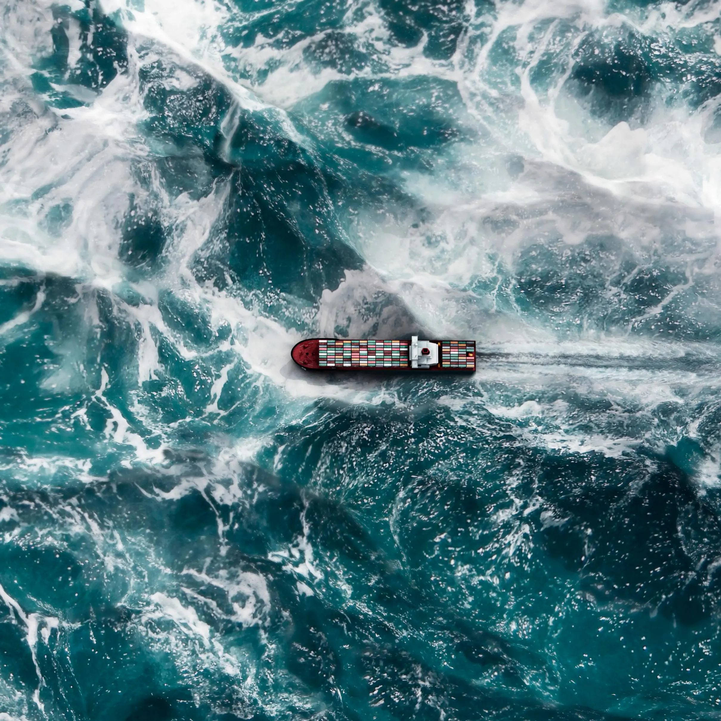 Aerial shot of a cargo ship sailing through choppy waters.